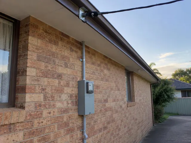 Brick house exterior with overhead service cable, point-of-attachment bracket and meter box on the wall in Toukley